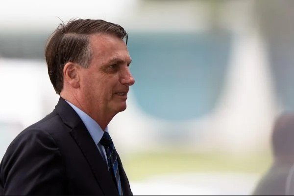 Bolsonaro aparece de perfil, usando terno e gravata, sem máscara, em algum do Palácio da Alvorada, lugar sorrindo - Metrópoles