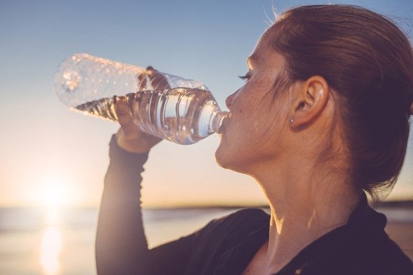 In the color image, a woman is positioned on the right side.  She wears a long T-shirt and is drinking from the neck of a bottle with clear liquid.