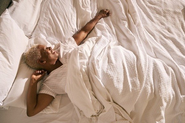 In the color image, a woman is positioned at the center.  She is lying on a bed with white sheets, wears a white nightgown and smiles as she looks to her right.