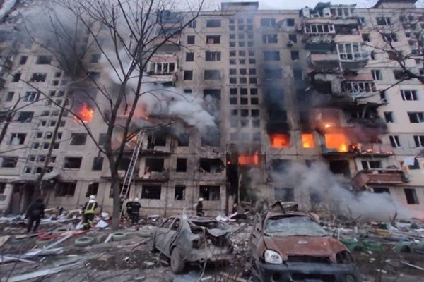 Prédio em chamas e cenário em frente destruido por bombardeios russos