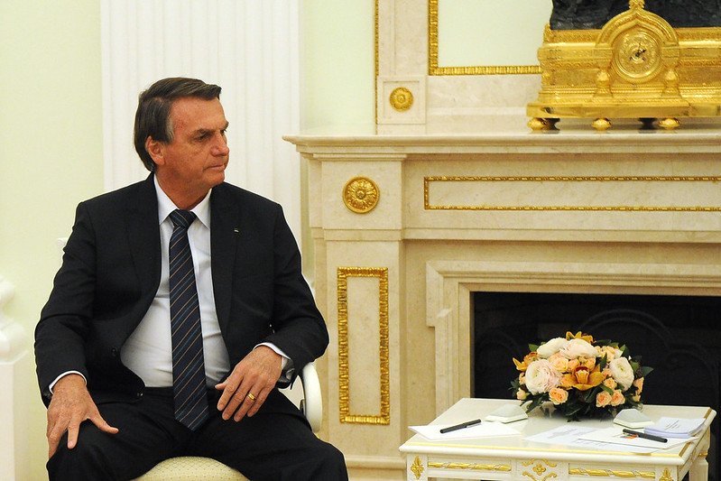 O presidente Bolsonaro (PL) se reúne com o presidente russo Vladimir Putin, num salão branco do Kremlin. Ele está de terno, sentado ao lado de uma mesa baixa - Metrópoles