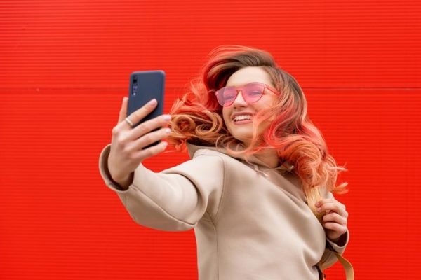 Mulher segurando celular em frente ao rosto em um fundo vermelho