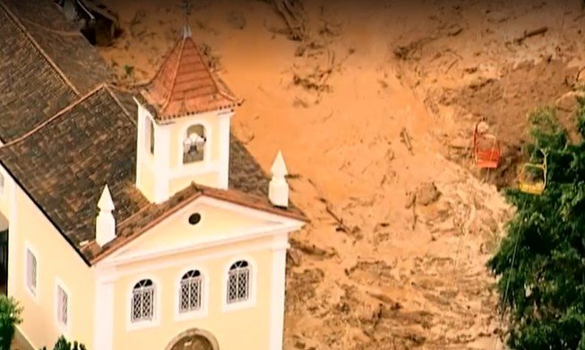 Na imagem colorida, lama está em cima de casas e arvores