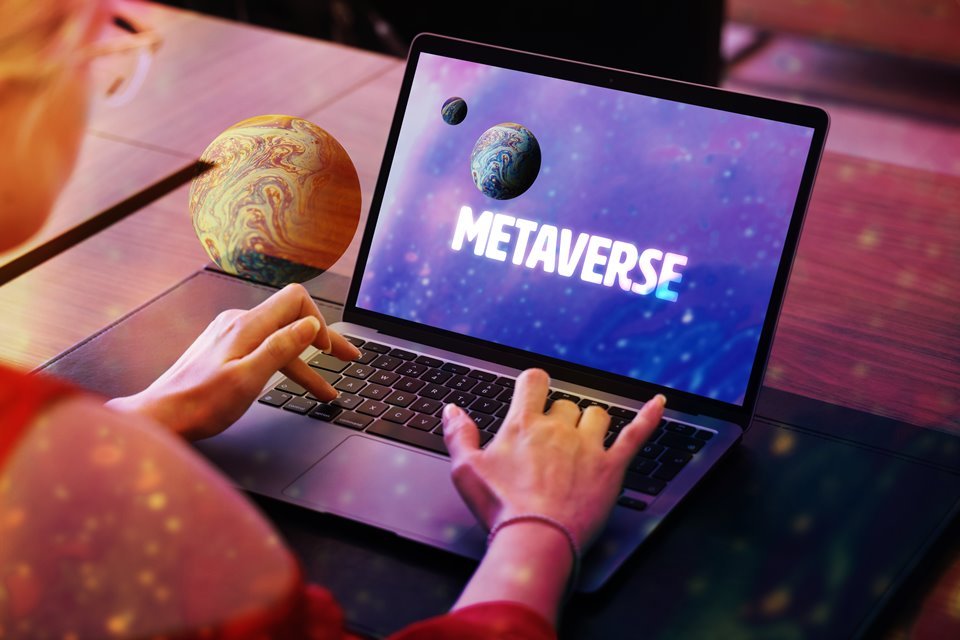 A woman types on a notebook.  The screen is labeled metaverse