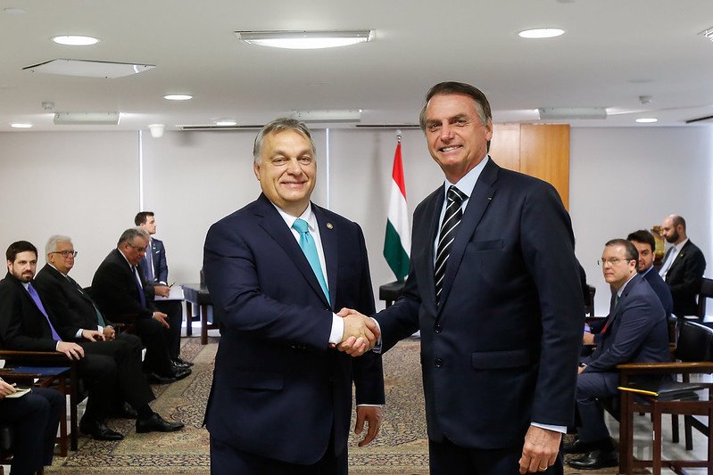 O presidente Jair Bolsonaro cumprimenta o líder da Hungria, Viktor Orbán, durante uma audiência em 2019. Ambos sorriem para foto, de terno, numa sala com outros homens ao fundo - Metrópoles