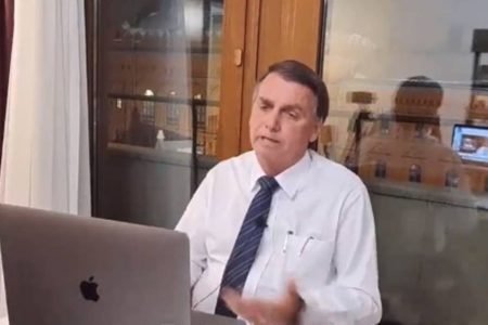 Bolsonaro dá entrevista para a Jovem Pan News. Ele está de frente para o computador com uma janela trás, vestindo camisa social e gravata - Metrópoles