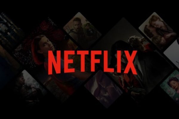 Logo da Netflix, na cor vermelha, em cima de um fundo preto com algumas capas de filme- Metrópoles