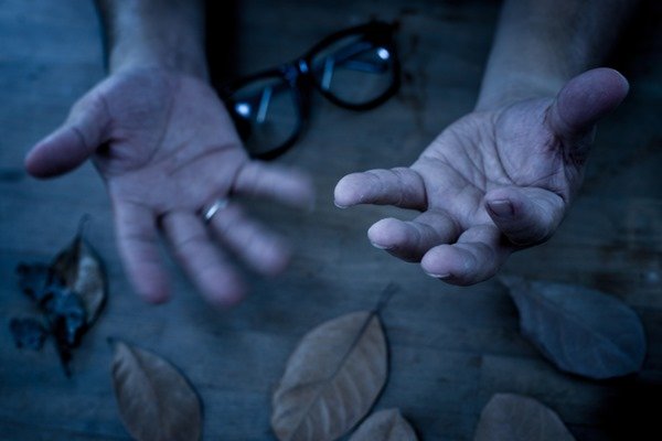 Mãos estão centralizadas e uma borra a imagem por tremer durante a fotografia. As mão são brancas e tem um óculos na mesa onde as mãos estão apoiadas