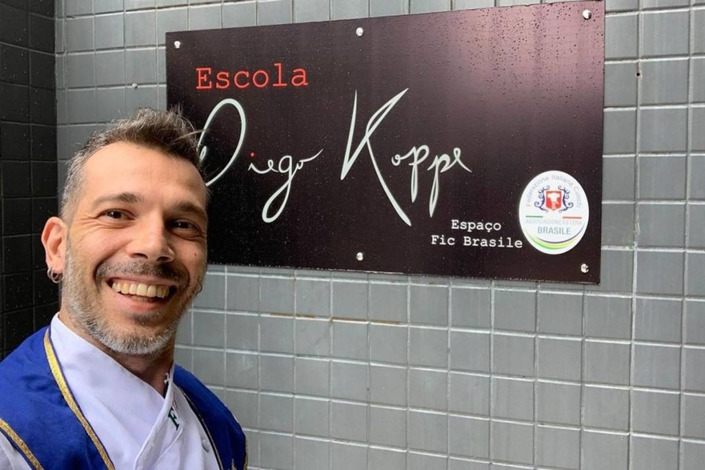 homem sorri em frente placa que diz escola diego koppe