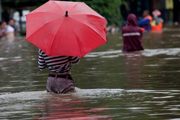 Homem anda em rua alagada com guarda-chuva vermelho na mão-Metrópoles