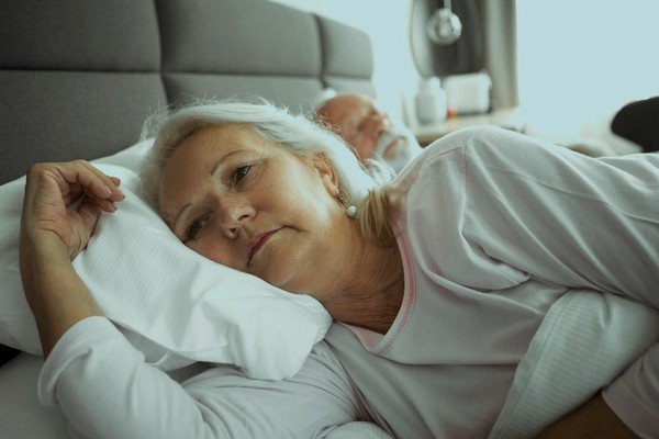 Elderly woman sharing a bed with a man.  She's lying on her side and can't sleep - Metropolis