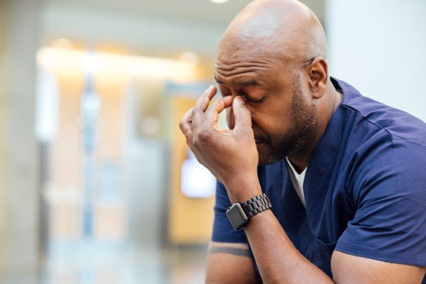 Homem aparenta estar estressado com a mão no rosto. Ele veste camiseta azul-Metrópoles