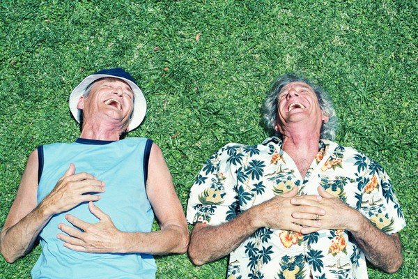 Elderly people lie side by side on the lawn and laugh