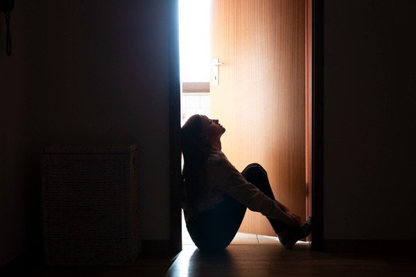 A woman is sitting on the floor with her legs folded.  She is near the door and looking at the ceiling - Metropolis