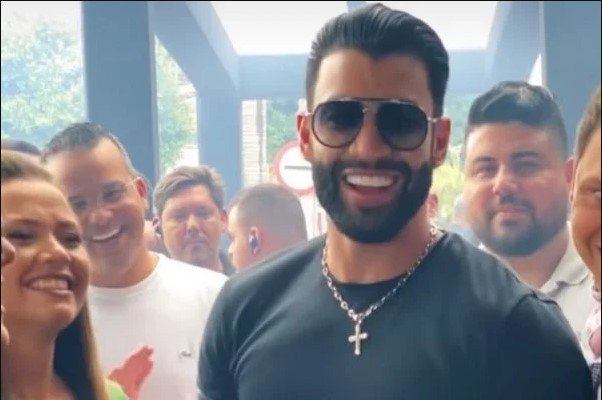 Gusttavo Lima cantor sertanejo em show. Ele tem cabelos pretos, barba preta e usa camisa preta