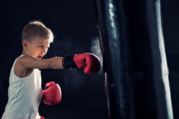 A boy practices boxing alone with red gloves