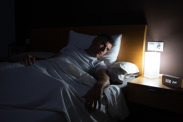 Man lying on bed next to bedside table with bright lights - Metropolis