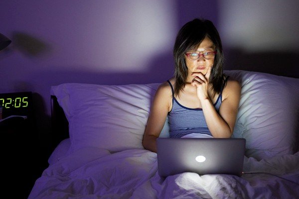 A woman sits in bed and uses a computer