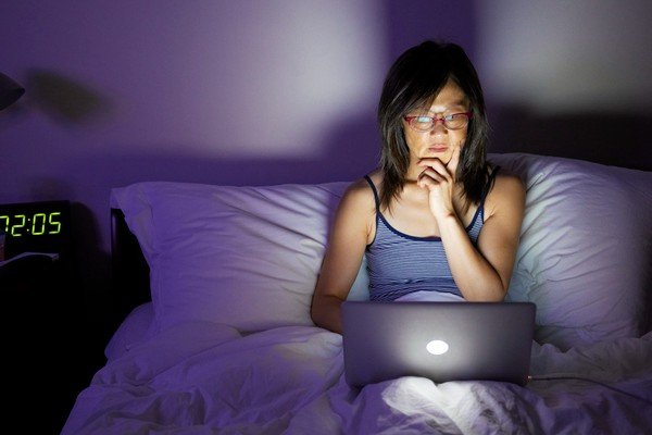 Woman sits on bed and uses computer - Metropolis