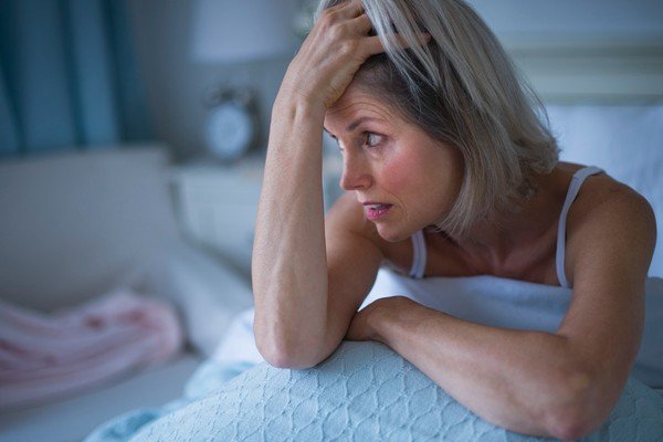 Woman sits on bed with insomnia.  She has her hand in her hair-Metropolises