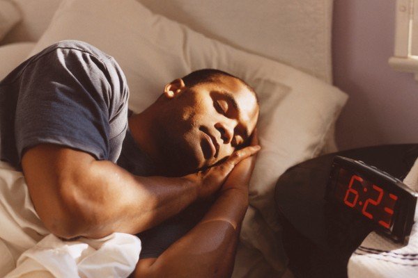 Man is sleeping in bed.  He is lying on his side next to the alarm clock in Metropolis