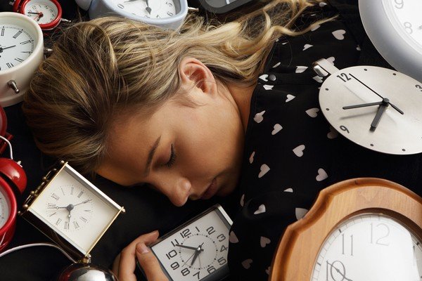 Woman sleeps surrounded by colorful alarm clocks - Metropolises