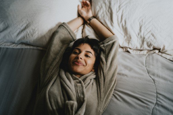 Woman lying on bed stretches with arms up - Metropolis