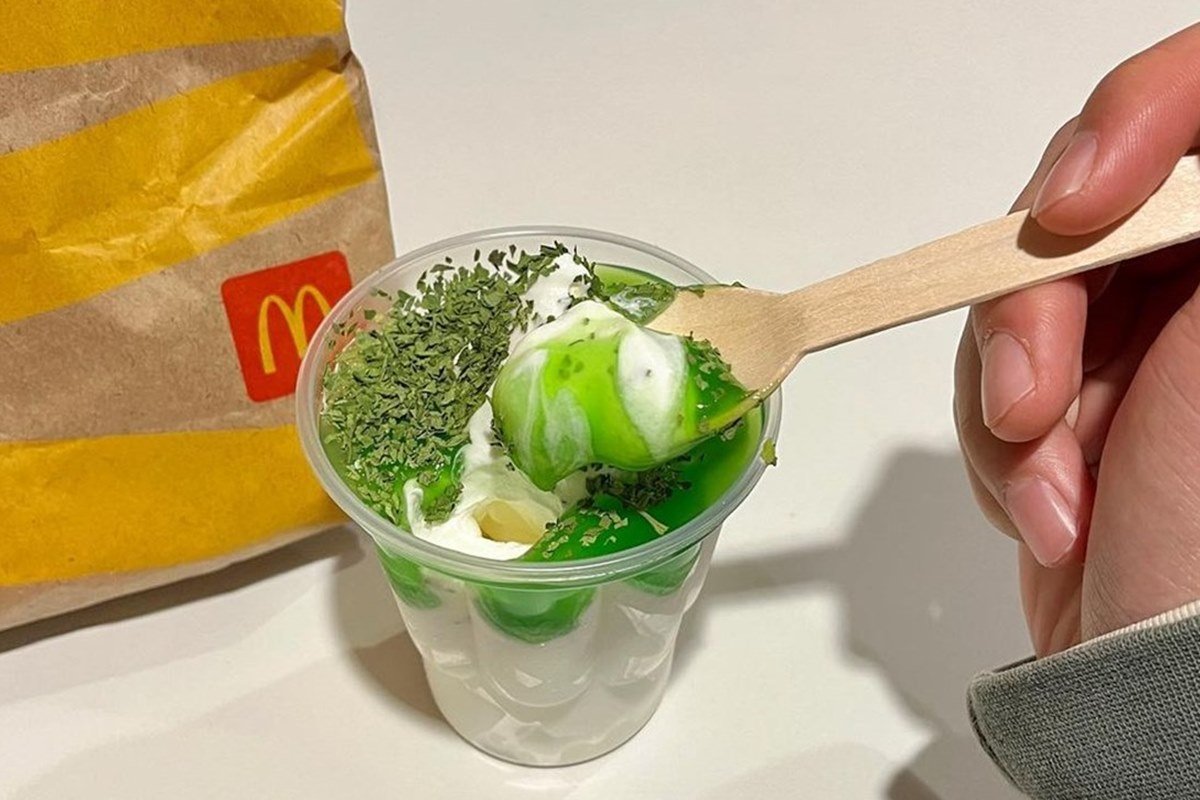 na foto temos um copo descartavel com sorvete branco e calda verde e coentro seco por cima