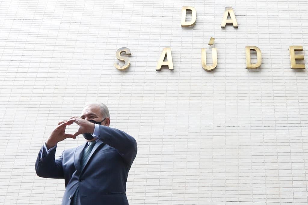 Na frente do Ministério da Saúde, o ministro Queiroga faz um gesto de coração com as mãos. Ele usa máscara e terno - Metrópoles