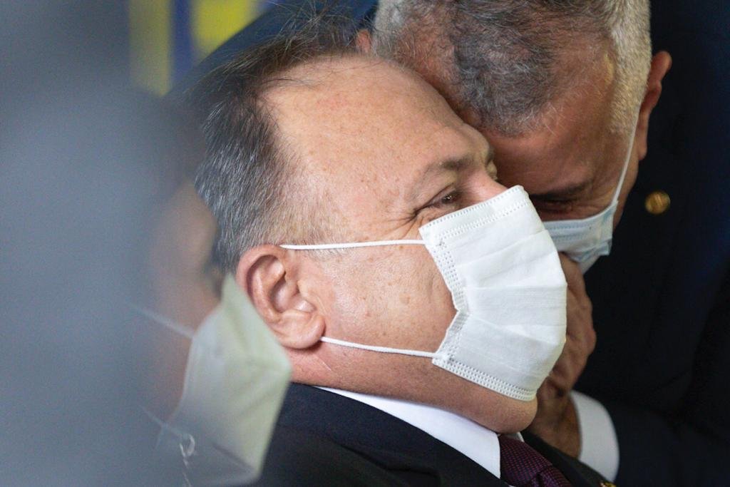 O general e ex-ministro Eduardo Pazuello em cerimônia de apresentação da primeira vacina 100% brasileira. Ele está sentado e alguém sussurra em seu ouvido, ao que ele ri - Metrópoles