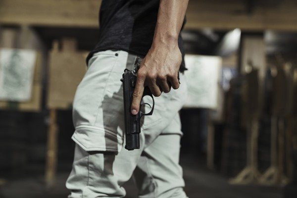Porte e porte de arma. Homem usando calça caqui e camiseta preta segurando uma arma de fogo na cor preta em uma das mãos- Metrópoles