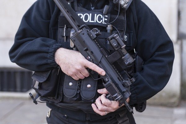 Porte e porte de arma. Pessoa com uniforme da polícia segurando uma arma de fogo na cor preta em uma das mãos- Metrópoles