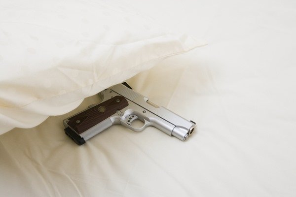 Arma de fogo em cima de uma cama com lençóis brancos- Metrópoles