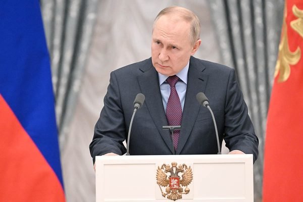 O presidente russo Vladimir Putin num discurso. Ele está frente a um púlpito, sob fundo neutro com a bandeira do país - Metrópoles
