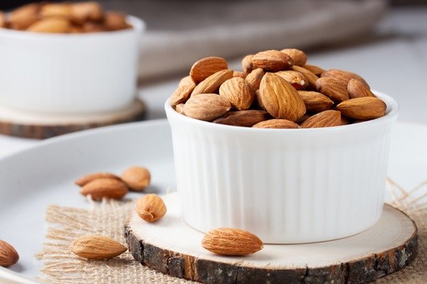 A white container with almonds is on top of a wooden surface and next to another container with almonds - Metropolis