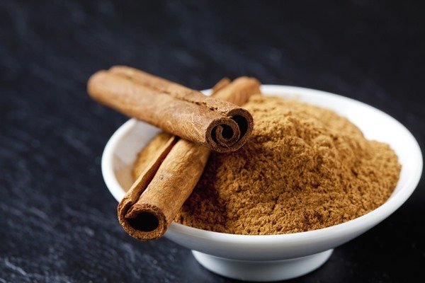 A white container with cinnamon powder is on top of a wooden surface - Metropolis