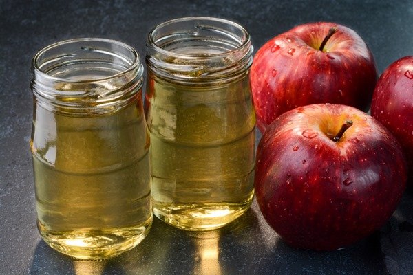 Glass jars filled with apple cider vinegar.  Next to the pots are red apples - Metrópoles