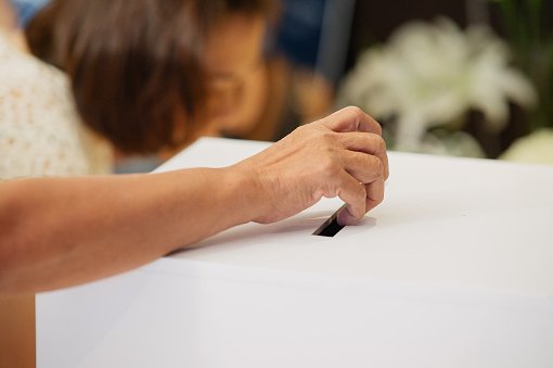 Mão de mulher negra inserindo cédula de papel com voto em urna