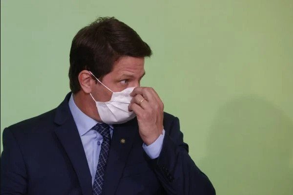 Mário Frias secretário de Cultura do governo Bolsonaro. Ele usa terno escuro, camiseta azul, gravata azul e está com uma das mãos na máscara branca que está no rosto- Metrópoles