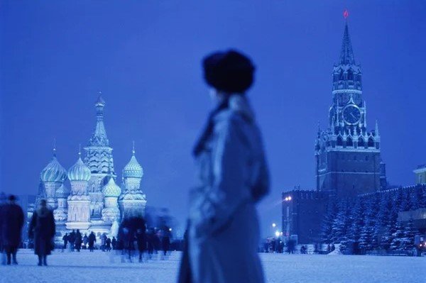 Na imagem colorida, o castelo de Moscou, na Russia está no fundo e uma pesso de lado e com roupas de frio ocupa o centro da imagem
