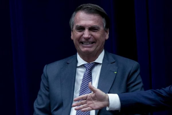 Bolsonaro ri em cerimônia de lançamento do Modelo Regulatório do Inmetro. Ele usa terno e está sem máscara - Metrópoles