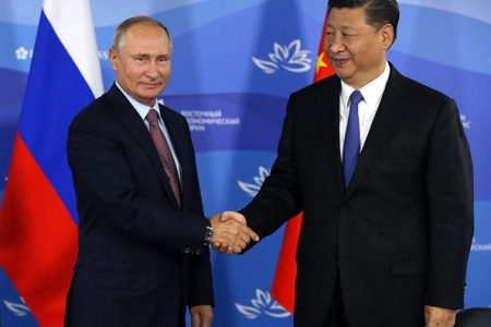 Presidente russo, Vladimir Putin e o presidente da China, Xi Jinping apertam as mãos em evento. Ao fundo estão as bandeiras russa e chinesa - Metrópoles