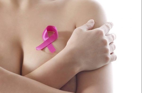 Mulher sem blusa segurando símbolo que representa luta contra o câncer de mama - Metrópoles