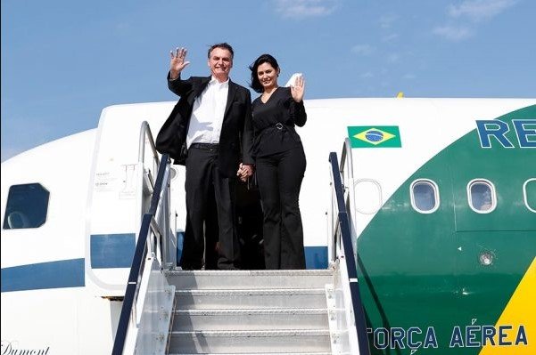 Bolsonaro e a esposa Michele Bolsonaro.  Eles estão saindo de uma aeronave da fab.  Usam roupas escuras e estão com as mãos levantadas saudando - Metropoles
