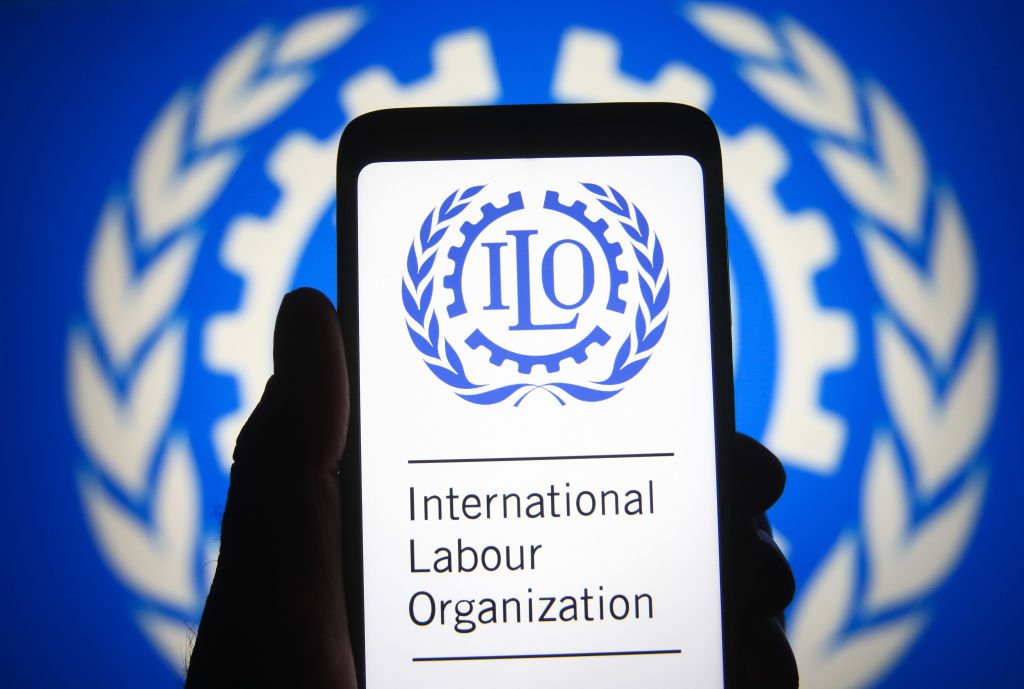 Aparelho com a imagem da Organização Internacional do Trabalho sendo segurado em frente a uma bandeira da instituição