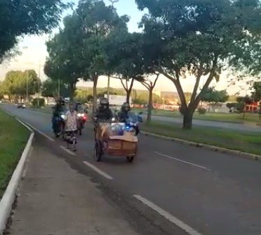 PM fardado empurrando carrinho com material reciclável caseiro, e PMs em moto na pista