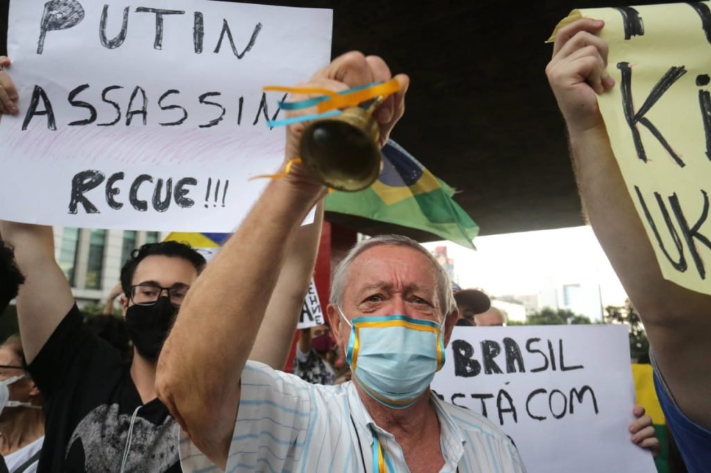 Comunidade ucraniana faz protesto no vão do MASP em São Paulo, na Avenida Paulista. Na imagem, homem usa máscara com cores da bandeira e segura sino - Metrópoles