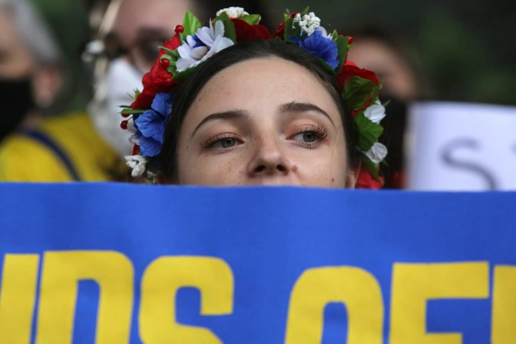 Em protesto da comunidade ucraniana em São Paulo, mulher com adereços típicos da Ucrânia segura cartaz - Metrópoles