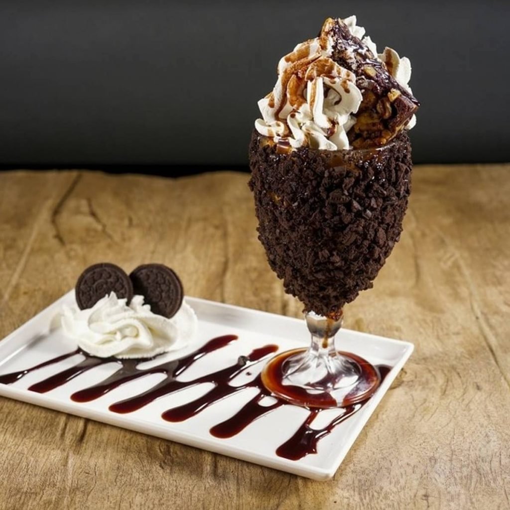 na foto temos um prato com uma taça melecada de chocolate e sorvete e chantilly no topo
