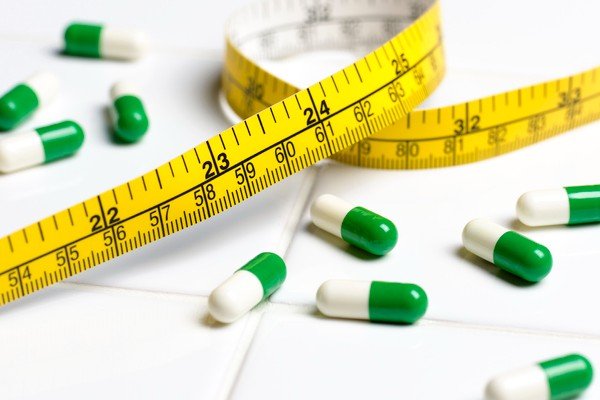 The picture shows a yellow measuring tape near green and white pills - Metropolis